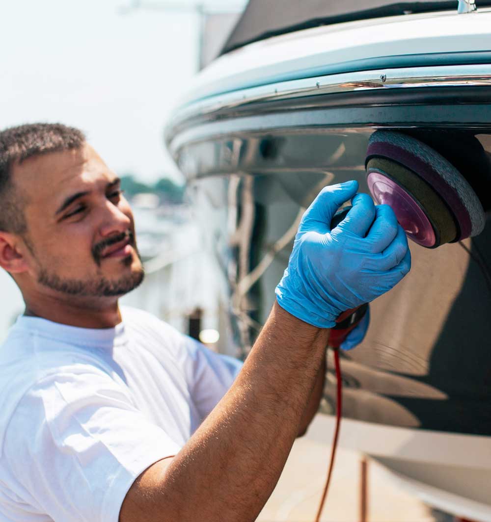 a man in gloves holding a power tool polishing a boat